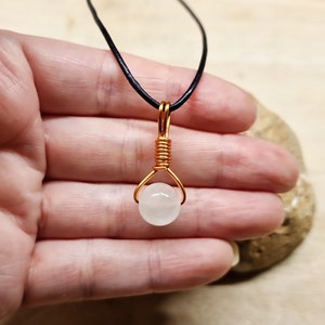 May include: A white gemstone pendant necklace with a copper wire wrap. The necklace is on a black leather cord.