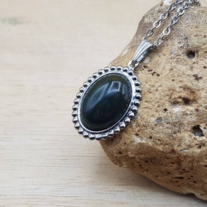 May include: A silver chain necklace with a dark green oval stone pendant set in a silver bezel with a beaded edge.