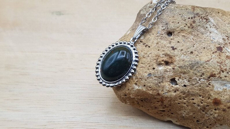 May include: A silver chain necklace with a dark green oval stone pendant set in a silver bezel with a beaded edge.