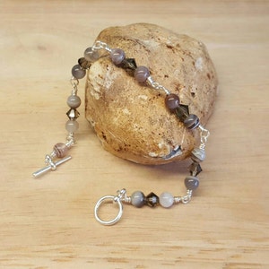May include: A silver bracelet with a toggle clasp features a mix of grey, brown, and white beads. The beads are a combination of round and faceted.