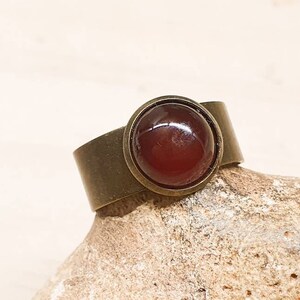 May include: A bronze ring with a round, red carnelian gemstone set in a bezel setting.