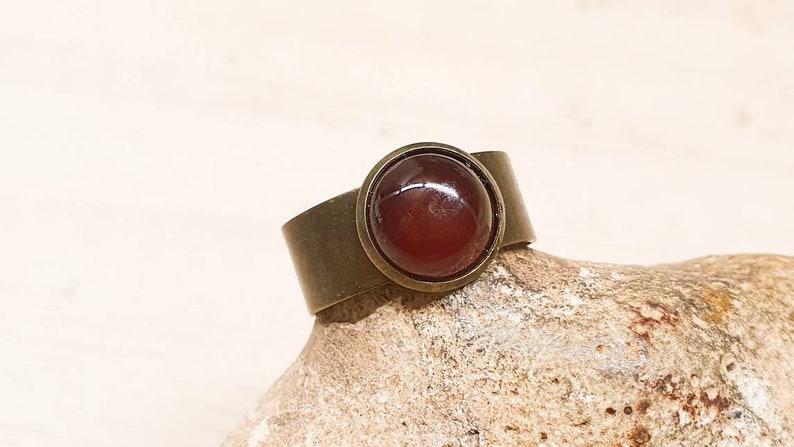 May include: A bronze ring with a round, red carnelian gemstone set in a bezel setting.