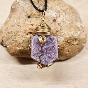 以下が含まれることがあります： 黒い紐に、金色のワイヤーで包まれた紫色の宝石のペンダントがぶら下がっている