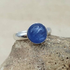 May include: A silver ring with a blue gemstone set in the center. The gemstone has a striated pattern.