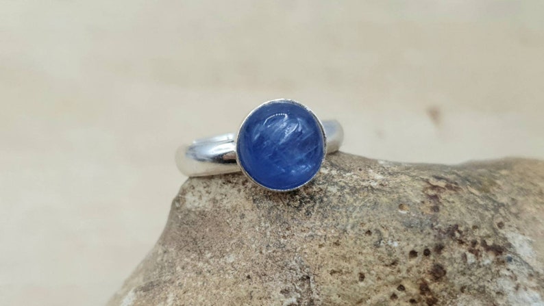 May include: A silver ring with a blue gemstone set in the center. The gemstone has a striated pattern.