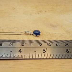 May include: A silver chain necklace with a blue gemstone pendant. The pendant is approximately 1.2 cm in diameter.