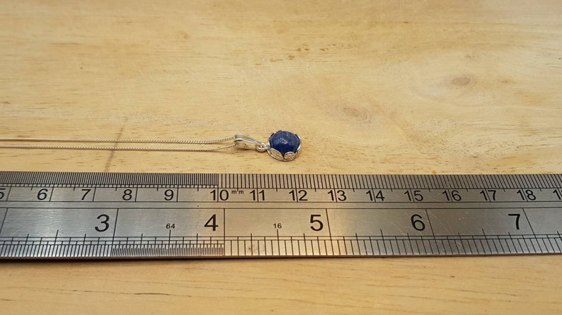 May include: A silver chain necklace with a blue gemstone pendant. The pendant is approximately 1.2 cm in diameter.