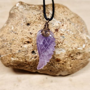 May include: A purple amethyst wing pendant with copper wire wrapping, hanging from a black cord.