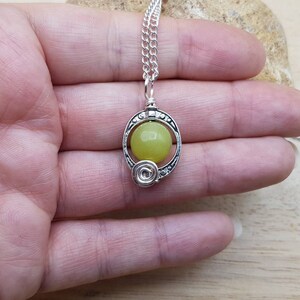 May include: A silver chain necklace with a pendant featuring a round, light yellow stone set in a silver frame with intricate details.