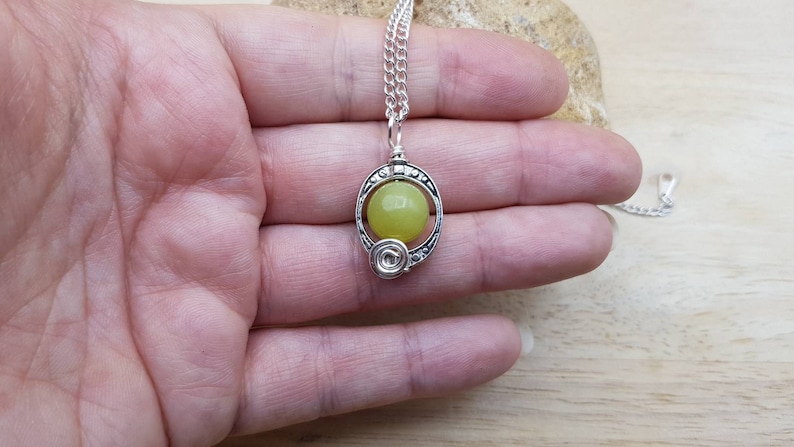 May include: A silver chain necklace with a pendant featuring a round, light yellow stone set in a silver frame with intricate details.