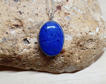 Könnte beinhalten: Eine silberne Halskette mit einem großen ovalen Anhänger aus blauem Lapislazuli.