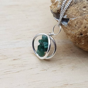 May include: A silver necklace with a pendant featuring a green gemstone encased in two silver circles.