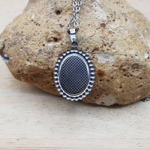 May include: A silver oval pendant with a textured surface and a beaded border. The pendant is attached to a silver chain.