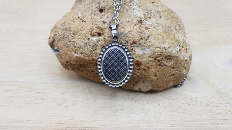May include: A silver oval pendant with a textured surface and a beaded border. The pendant is attached to a silver chain.