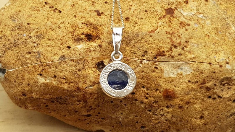 May include: A silver pendant necklace with a round blue stone set in a silver bezel. The pendant is inscribed with the words "925 Sterling Silver".