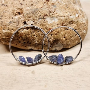 May include: Silver hoop earrings with three small blue gemstones on each hoop.