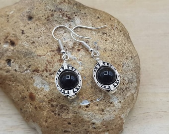 May include: A pair of silver dangle earrings with black oval-shaped stones set in ornate silver frames.
