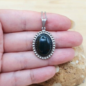 May include: A silver oval pendant necklace with a dark green gemstone. The pendant has a beaded border.