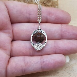 May include: A silver necklace with a brown stone pendant in a circular design. The pendant has a swirl design on the bottom.