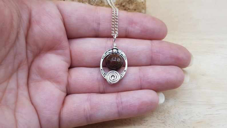 May include: A silver necklace with a brown stone pendant in a circular design. The pendant has a swirl design on the bottom.
