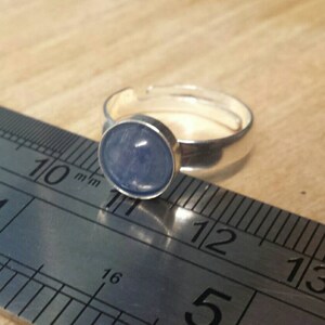 May include: A silver ring with a light blue cabochon gemstone. The ring is measured against a ruler, with the stone measuring approximately 11 mm in diameter.