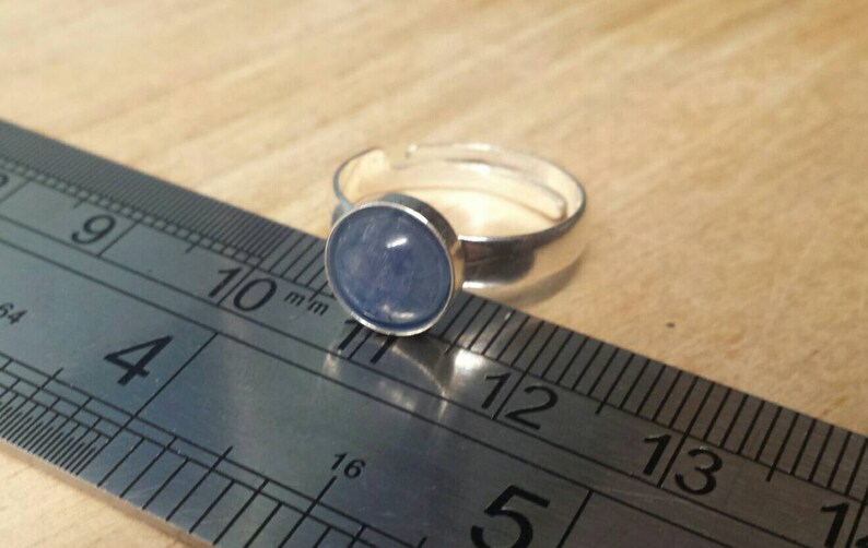 May include: A silver ring with a light blue cabochon gemstone. The ring is measured against a ruler, with the stone measuring approximately 11 mm in diameter.