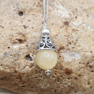 Puede incluir: Un collar con un colgante de plata adornado con una piedra preciosa amarilla y un dise&ntilde;o de plata ornamentado. El colgante cuelga de una cadena de plata.