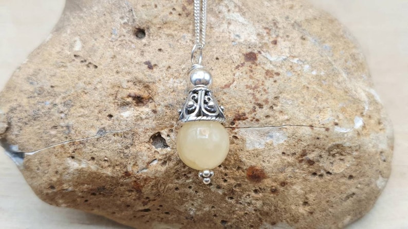 Puede incluir: Un collar con un colgante de plata adornado con una piedra preciosa amarilla y un dise&ntilde;o de plata ornamentado. El colgante cuelga de una cadena de plata.