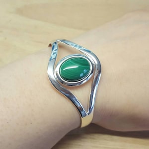 May include: A silver bracelet with a green malachite stone set in the centre. The bracelet is shaped like an eye.