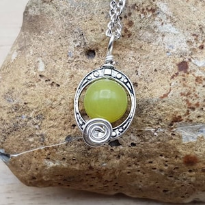 May include: A silver pendant necklace with a green jade stone set in a decorative silver frame. The pendant is hanging from a silver chain.