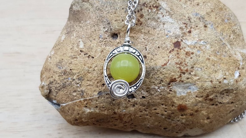 May include: A silver pendant necklace with a green jade stone set in a decorative silver frame. The pendant is hanging from a silver chain.