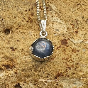 May include: A silver chain necklace with a pendant featuring a round, dark blue gemstone set in a silver frame.