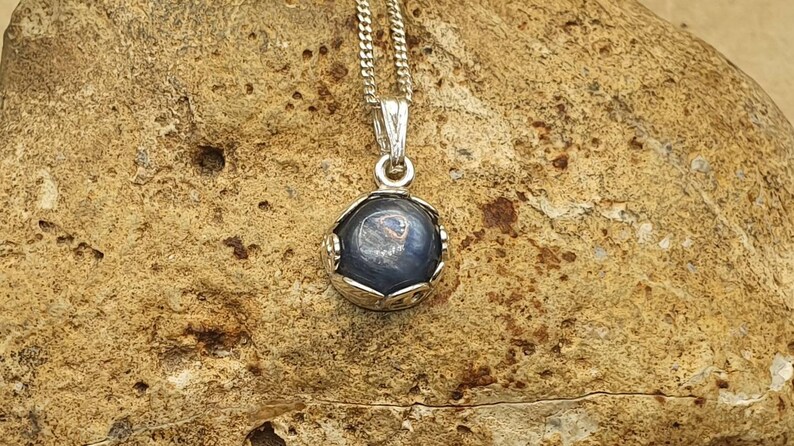 May include: A silver chain necklace with a pendant featuring a round, dark blue gemstone set in a silver frame.