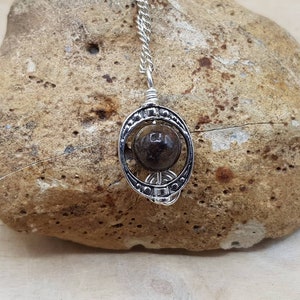 May include: A silver pendant necklace with a dark brown stone set in a circular cage design.