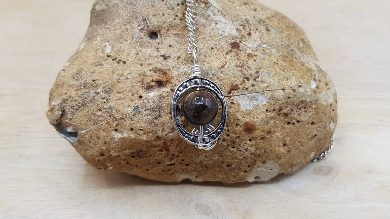 May include: A silver pendant necklace with a dark brown stone set in a circular cage design.