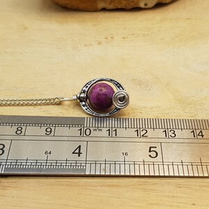 K&ouml;nnte beinhalten: Eine silberne Halskette mit einem Anh&auml;nger aus rosa und wei&szlig;em Stein. Der Anh&auml;nger ist eine Kugel mit einem silbernen Drahtdesign darum herum. Die Halskette wird an einem Lineal gemessen und ist etwa 10 cm lang.