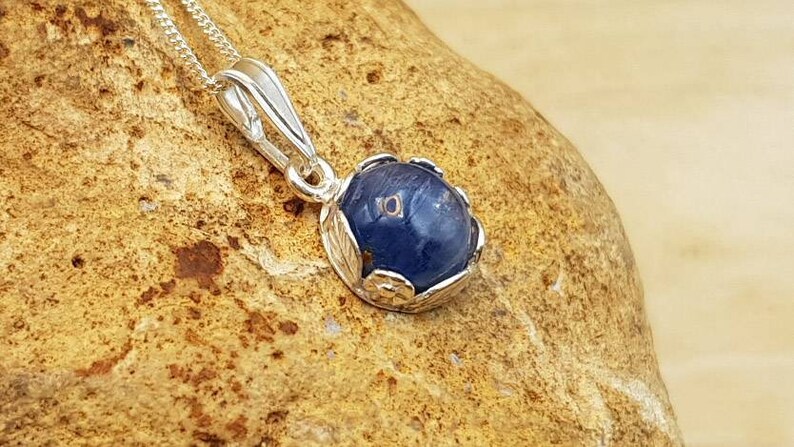 May include: A silver pendant necklace with a blue gemstone set in a silver floral design.