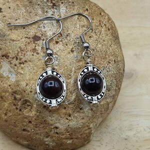 May include: A pair of silver earrings with a dark red gemstone in each. The earrings have a detailed, ornate design.