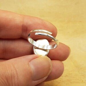 May include: Silver adjustable ring with a smooth oval-shaped setting. The ring is open at the back and has a simple design.