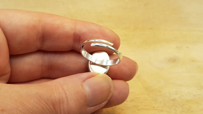 May include: Silver adjustable ring with a smooth oval-shaped setting. The ring is open at the back and has a simple design.