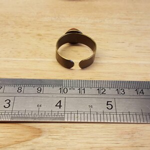 May include: A brass ring with a gap in the back, measured against a ruler. The ring is 10 mm wide.