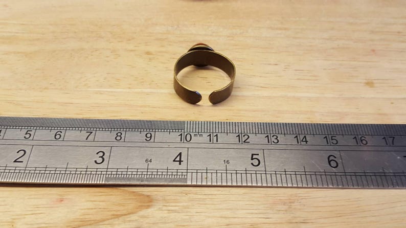 May include: A brass ring with a gap in the back, measured against a ruler. The ring is 10 mm wide.