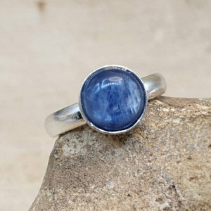May include: A silver ring with a round blue gemstone. The ring is set on a rough, brown rock.