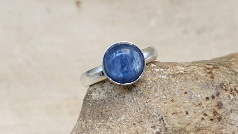 May include: A silver ring with a round blue gemstone. The ring is set on a rough, brown rock.