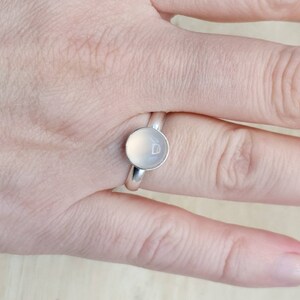 May include: A silver ring with a round, white stone set in the center. The stone has a small, engraved heart on it.