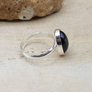 May include: A silver adjustable ring with a black oval gemstone.