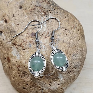 May include: A pair of silver earrings with a light green stone set in a silver frame. The earrings have a hook fastening.