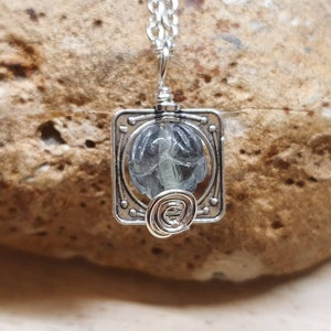 May include: A silver pendant necklace with a square frame and a clear glass stone inside. The stone has a swirling pattern inside.