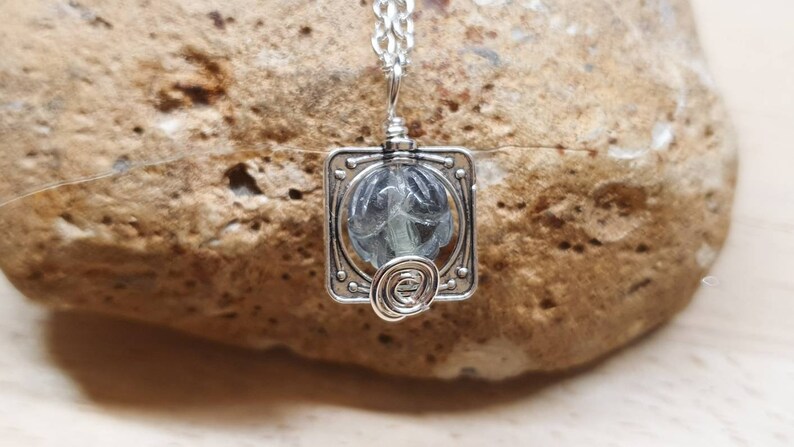 May include: A silver pendant necklace with a square frame and a clear glass stone inside. The stone has a swirling pattern inside.