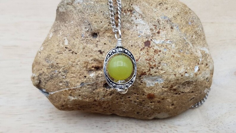 May include: A silver chain necklace with a pendant featuring a round, light green stone set in a silver frame.